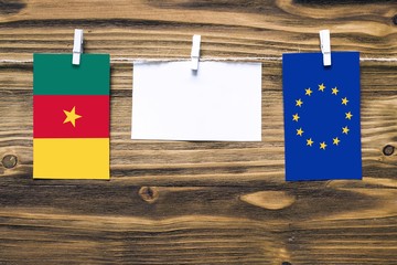 Hanging flags of Cameroon and European Union attached to rope with clothes pins with copy space on white note paper on wooden background.Diplomatic relations between countries.