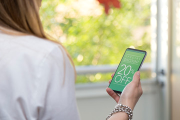 20% off Promotion, special discount in a cell phone. One young woman holding a smartphone with a...