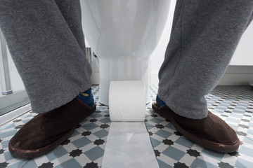 Pies de un hombre en el baño con papel higiénico