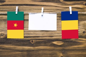 Hanging flags of Cameroon and Romania attached to rope with clothes pins with copy space on white note paper on wooden background.Diplomatic relations between countries.