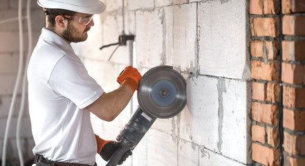 The industrial Builder works with a professional angle grinder to cut bricks and build interior walls. Electrician.