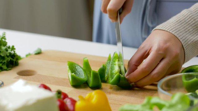 healthy eating, vegetarian food and cooking concept - young woman with kitchen knife chopping vegetables on wooden cutting board at home