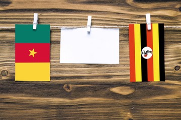 Hanging flags of Cameroon and Uganda attached to rope with clothes pins with copy space on white note paper on wooden background.Diplomatic relations between countries.