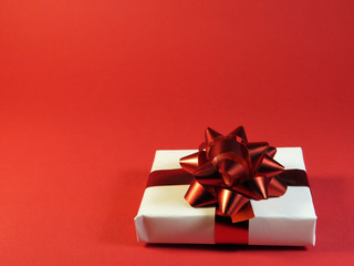 White gift box with a red ribbon on a red background. Celebration, congratulations. Designs for invitations, greeting cards.