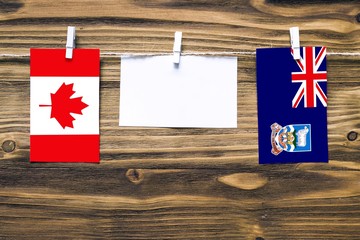 Hanging flags of Canada and Falkland Islands attached to rope with clothes pins with copy space on white note paper on wooden background.Diplomatic relations between countries.