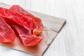 Four pieces of dried passion fruit in sugar lie on a food bag on a white wooden background, top view from the side