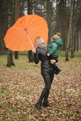 a beautiful Caucasian mother and little child having fun in autumn Park, walking with umbrella