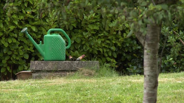 Wide shot of a green plastic watering can and a pair of hedge trimmers sitting on a stone well cover