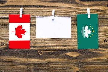 Hanging flags of Canada and Macao attached to rope with clothes pins with copy space on white note paper on wooden background.Diplomatic relations between countries.