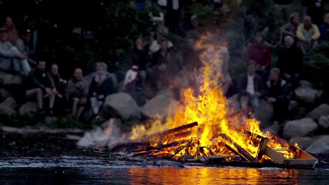 View of a Large Bonfire Burning by the Water and People Sitting at Background