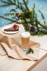 Delicious fresh festive morning cappuccino coffee in a glass cup and cupcake dessert on the wooden table, fireflies and spruce branches