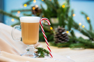 Delicious cappuccino coffee cup and Christmas candy sweet. fireflies and spruce branches background.