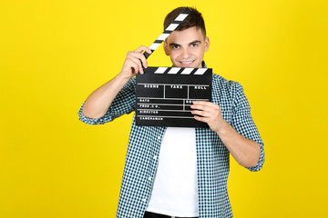 Young man with black clapper board on yellow background