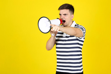 Young man screaming in megaphone on yellow background
