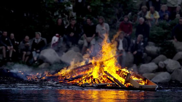 Medium Shot of a Pile of Wood Burning with High Flames by the River Bank