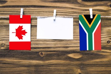 Hanging flags of Canada and South Africa attached to rope with clothes pins with copy space on white note paper on wooden background.Diplomatic relations between countries.