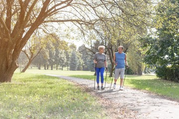Obraz premium Senior couple with hiking poles walking on footpath in park