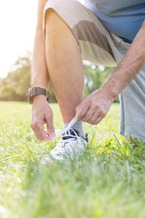 Obraz na płótnie Canvas Low section of senior jogger tying shoelace on grassy field