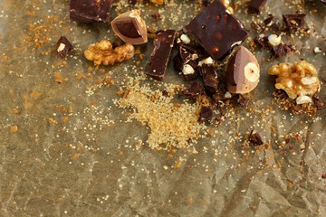 Sweets, pieces of chocolate and nuts, cane sugar on a non-uniform beige background.