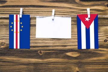 Hanging flags of Cape Verde and Cuba attached to rope with clothes pins with copy space on white note paper on wooden background.Diplomatic relations between countries.