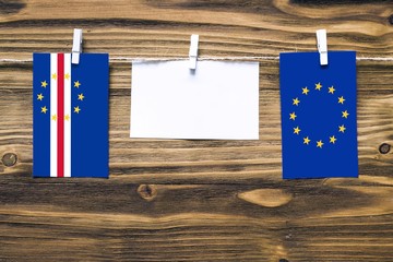 Hanging flags of Cape Verde and European Union attached to rope with clothes pins with copy space on white note paper on wooden background.Diplomatic relations between countries.