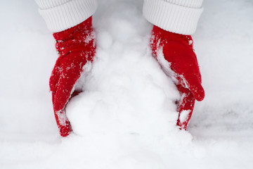 Girl's hands in red gloves making snowball