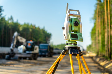 Surveyor engineer with equipment (theodolite or total positioning station) on the construction site of the road or building with construction machinery background