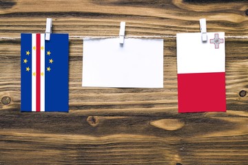 Hanging flags of Cape Verde and Malta attached to rope with clothes pins with copy space on white note paper on wooden background.Diplomatic relations between countries.