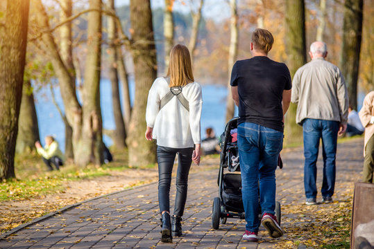 A Married Couple Rolls A Baby Stroller In A City Park 