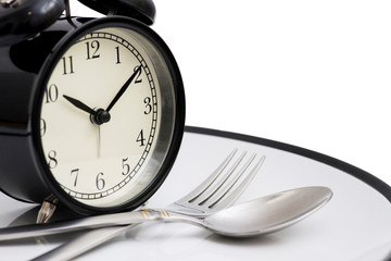 Black alarm clock with fork and knife on the plate. Isolated on white. Time to eat. Weight loss or...