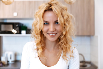 At home. Woman portrait. Blonde girl is looking at camera and smiling; in the kitchen