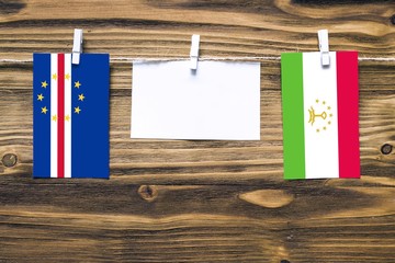 Hanging flags of Cape Verde and Tajikistan attached to rope with clothes pins with copy space on white note paper on wooden background.Diplomatic relations between countries.