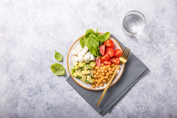 Buddha Bowl with Avocado, chickpea, feta cheese, fresh spinach, Tomatoes and glass of water. Concept for healthy vegetarian detox balanced meal. Top view. Copy space.