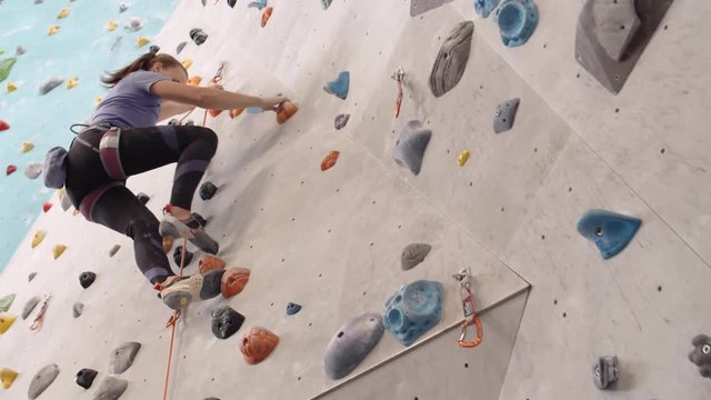 Low angle view of young slim sportswoman wearing safety equipment climbing wall in gym