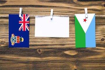 Hanging flags of Cayman Islands and Djibouti attached to rope with clothes pins with copy space on white note paper on wooden background.Diplomatic relations between countries.