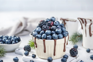 Chocolate mug cake with blueberries and blackberries in a white ceramic mug on white background