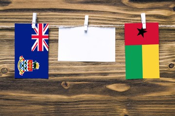 Hanging flags of Cayman Islands and Guinea Bissau attached to rope with clothes pins with copy...