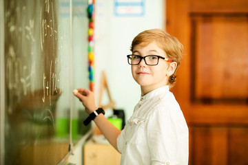 Elementary school student with black glasses writing maths answer on chalkboard