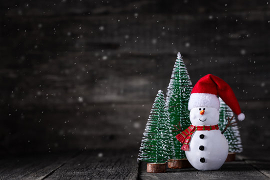 Snowman toy in Santa Claus hat and New Year tree on wooden rustic background