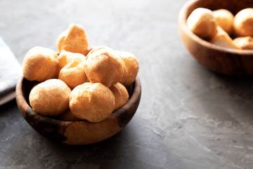 Round small fresh homemade eclairs or profiteroles in a wooden round cup on a dark background. In the background, eclairs in a cup out of focus
