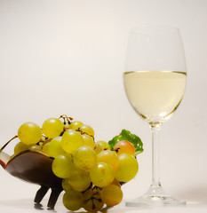  Beautiful stylish still life - a glass with white wine and a vase with grapes on a light background
