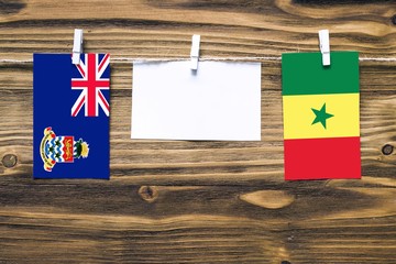 Hanging flags of Cayman Islands and Senegal attached to rope with clothes pins with copy space on white note paper on wooden background.Diplomatic relations between countries.