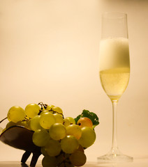  Still life of a glass with champagne and white grapes in a vase on a light background