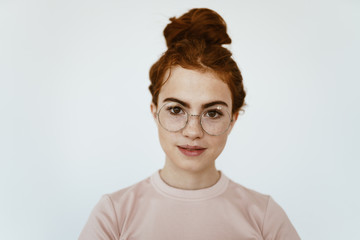 a schoolgirl with glasses, with a smart look, stands in a light-colored studio