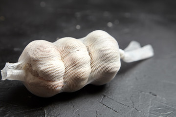 Garlic heads in a mesh bag on black stone background. Packed whole white garlic bulbs on dark table closeup. Spice with pungent flavor, seasoning, condiment