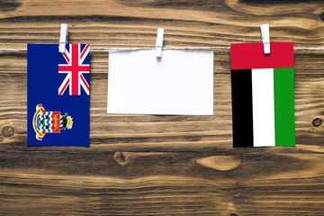 Hanging flags of Cayman Islands and United Arab Emirates attached to rope with clothes pins with copy space on white note paper on wooden background.Diplomatic relations between countries.