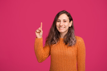 Portrait of smiling woman in sweeater pointing up at copyspace