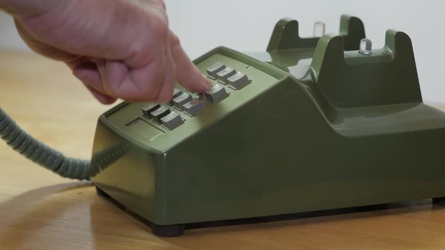 Man dialing retro push button rotary dial telephone. Making phone call on vintage avocado green landline phone.