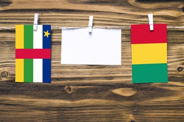 Hanging flags of Central African Republic and Guinea attached to rope with clothes pins with copy space on white note paper on wooden background.Diplomatic relations.