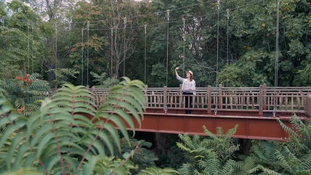 Millennial hipster woman tourist using smartphone making selfie on the bridge in the rainforest jungle.